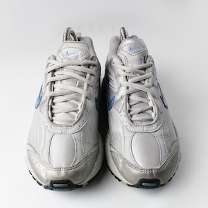 May include: A pair of white athletic shoes with blue accents. The shoes have a mesh and leather upper and a white rubber sole.
