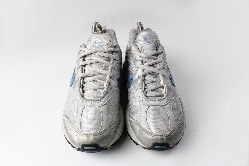 May include: A pair of white athletic shoes with blue accents. The shoes have a mesh and leather upper and a white rubber sole.