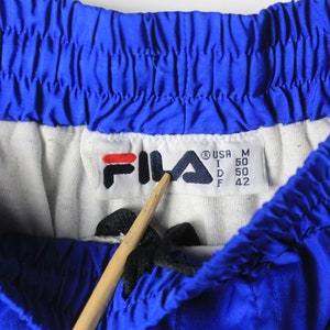 May include: A blue Fila brand athletic shorts with a white waistband and a size tag that reads "USA M I 50 D 50 F 42".