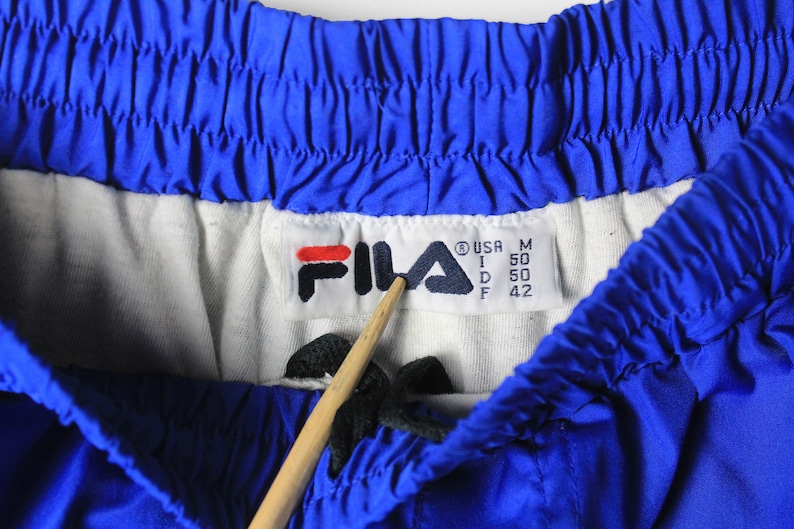 May include: A blue Fila brand athletic shorts with a white waistband and a size tag that reads "USA M I 50 D 50 F 42".