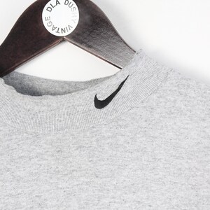 May include: A gray mock neck t-shirt with a black Nike swoosh logo on the front.