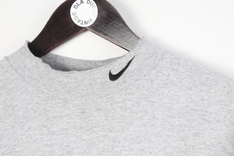 May include: A gray mock neck t-shirt with a black Nike swoosh logo on the front.