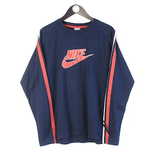 May include: A navy blue long-sleeved shirt with red and white stripes on the sleeves. The shirt features a large red Nike logo with the word "NIKE" in white.