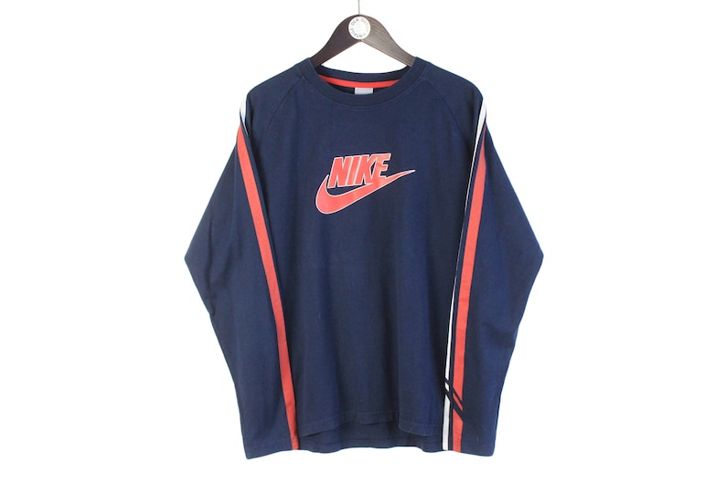 May include: A navy blue long-sleeved shirt with red and white stripes on the sleeves. The shirt features a large red Nike logo with the word "NIKE" in white.