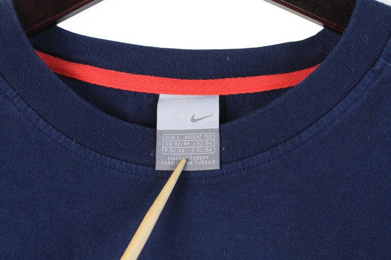 May include: A navy blue t-shirt with a white tag that reads "Size L Height 183 GB 42/44 F 52/54 I 52/54 Made in Turkey Fabrique en Turquie".