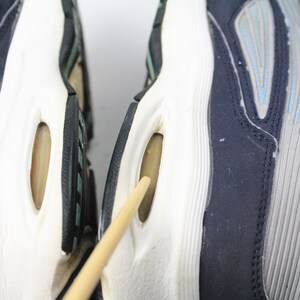 May include: Close-up of the bottom of two blue and gray running shoes with white soles. The shoes have a unique design with air pockets in the soles.