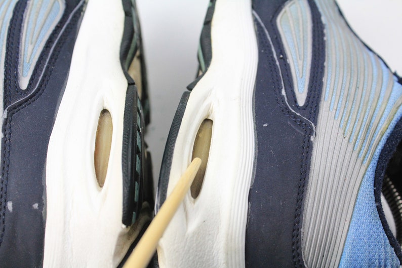May include: Close-up of the bottom of two blue and gray running shoes with white soles. The shoes have a unique design with air pockets in the soles.
