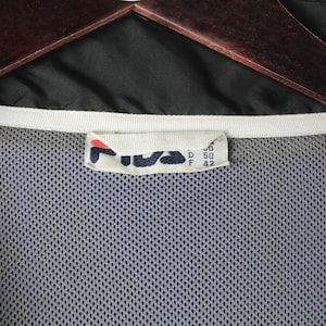 May include: A black Fila windbreaker jacket with a white zipper and a mesh lining. The size tag reads "M, D 50, F 42".