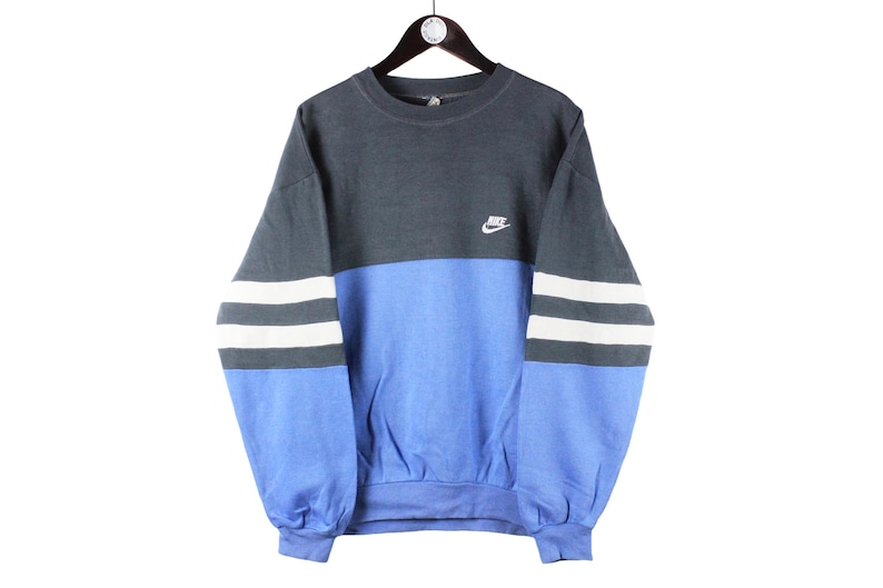 May include: A blue and gray sweatshirt with white stripes on the sleeves. The sweatshirt has a Nike logo on the front.