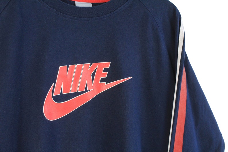 May include: A navy blue sweatshirt with red and white stripes on the sleeves. The sweatshirt features a large red Nike logo with the word "NIKE" in white.