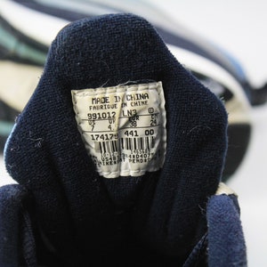 May include: A white tag with black text on a blue shoe. The tag reads "Made in China, Fabrique in Chine, 991012 LN3, US 7 UP 4, UR 38 CH 24, 174179 441 00, 10-12 1465689 3143040754".