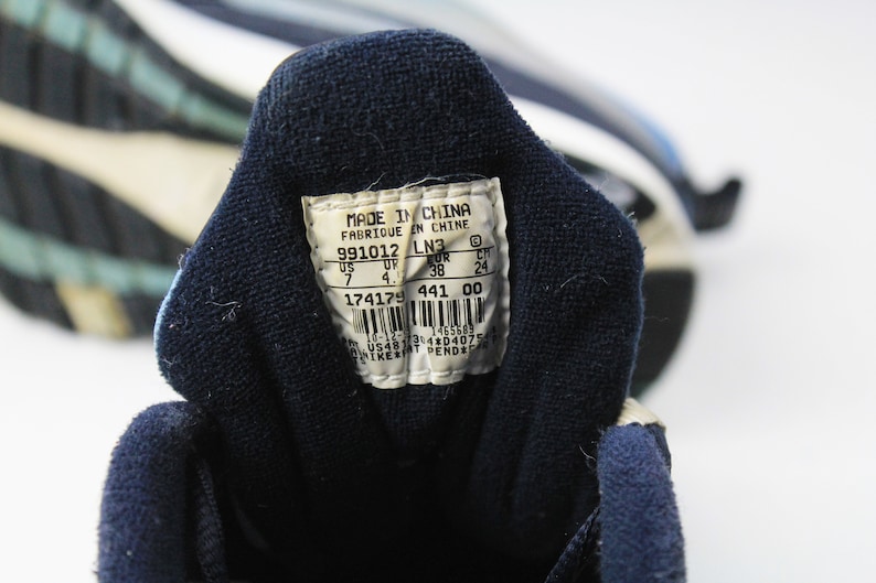 May include: A white tag with black text on a blue shoe. The tag reads "Made in China, Fabrique in Chine, 991012 LN3, US 7 UP 4, UR 38 CH 24, 174179 441 00, 10-12 1465689 3143040754".