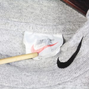 May include: Gray t-shirt with a black Nike swoosh logo and a white Nike tag with red lettering.