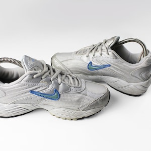 May include: A pair of gray athletic shoes with blue and green accents. The shoes have a white sole and a lace-up closure.