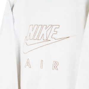 May include: White long-sleeve shirt with a brown outline of the Nike logo and the text "NIKE AIR" on the front.