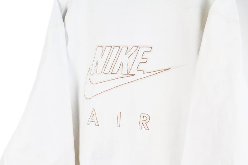 May include: White long-sleeve shirt with a brown outline of the Nike logo and the text "NIKE AIR" on the front.