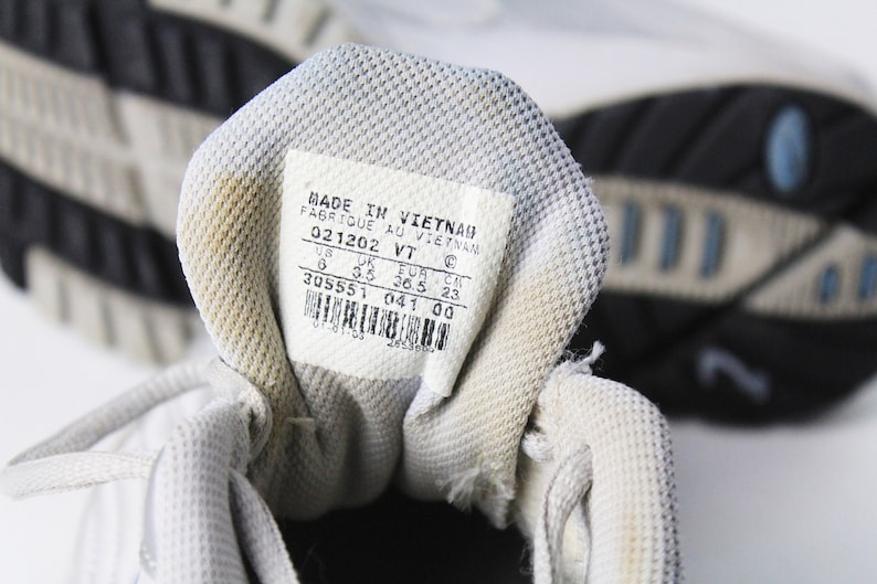 May include: Close-up of the inside of a white athletic shoe with a white label that reads "MADE IN VIETNAM FABRIQUE AU VIETNAM 021202 VT 6 3.5 36.5 23 EUR CM 305551 041 00".