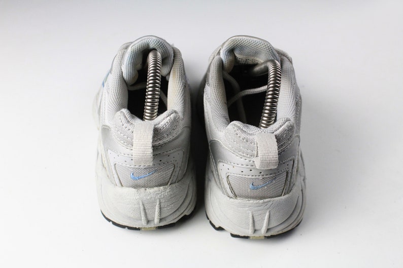 May include: A pair of white athletic shoes with blue accents. The shoes have a mesh and leather upper and a thick rubber sole.