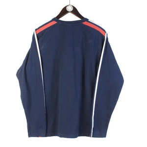 May include: A navy blue long-sleeved shirt with white and red trim on the sleeves.