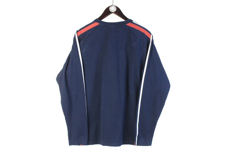 May include: A navy blue long-sleeved shirt with white and red trim on the sleeves.