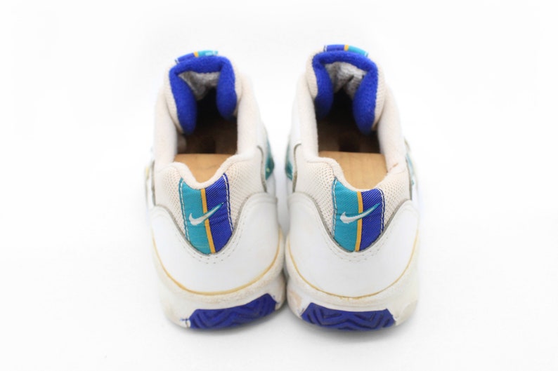 May include: A pair of white leather sneakers with blue and teal accents. The sneakers have a white swoosh logo on the side and a blue and yellow stripe on the back.