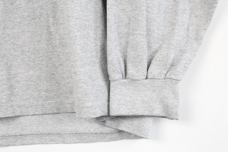 May include: Close-up of the gray fabric cuff of a long-sleeve shirt. The cuff is folded over and stitched.