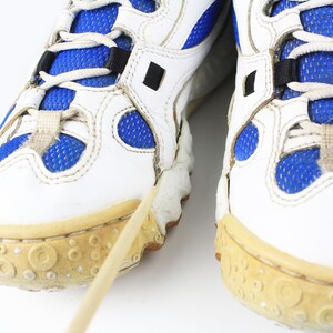 Może przedstawiać: Para białych but&oacute;w sportowych z niebieskimi wstawkami z siateczki i białymi sznurowadłami. Buty mają grubą, fakturowaną podeszwę.