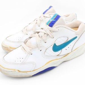 May include: White leather sneakers with blue and yellow accents and a blue Nike swoosh logo.