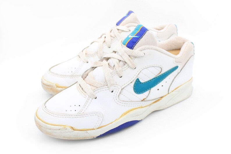 May include: White leather sneakers with blue and yellow accents and a blue Nike swoosh logo.