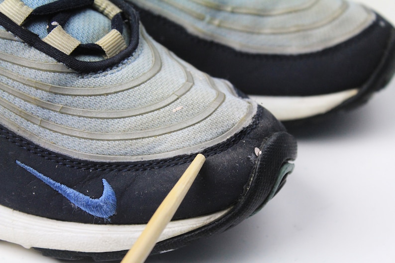 May include: Close-up of a pair of blue and black Nike Air Max 97 sneakers. The shoes have a mesh and leather upper with a white midsole and black outsole. The Nike swoosh logo is visible on the side of the shoe.