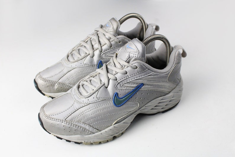 May include: A pair of silver athletic shoes with blue accents and a Nike swoosh logo. The shoes have a textured sole and a lace-up closure.