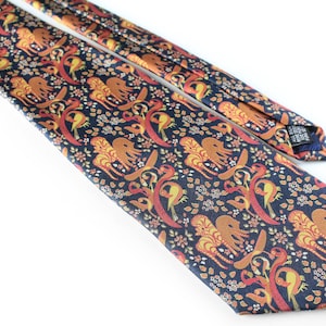 Pode incluir: Uma gravata de seda azul escura com um padrão repetido de pássaros e elefantes estilizados laranja, amarelo e vermelho sobre um fundo azul marinho.