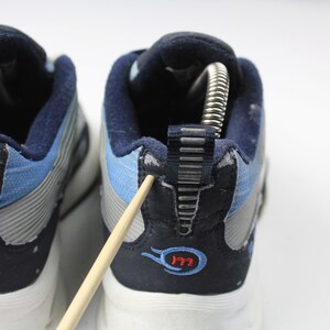 May include: A pair of blue and gray sneakers with a white sole. The back of the shoes have a blue and gray fabric with a silver zipper detail. The shoes have a red and blue logo that says "177".