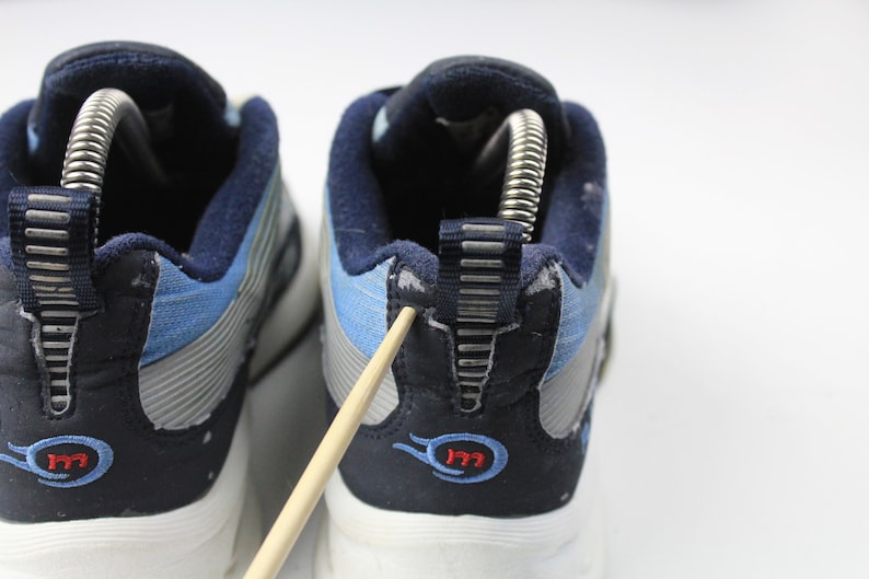 May include: A pair of blue and gray sneakers with a white sole. The back of the shoes have a blue and gray fabric with a silver zipper detail. The shoes have a red and blue logo that says "177".