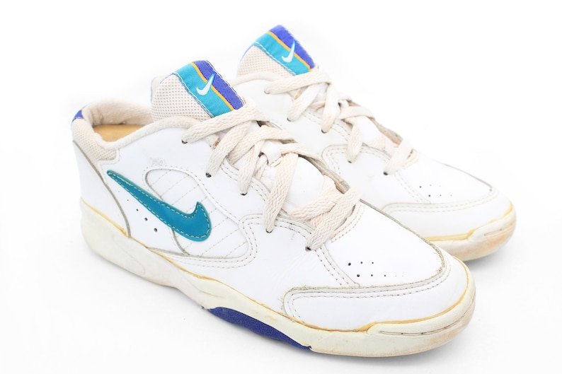 May include: White leather sneakers with blue and yellow accents. The sneakers have a white sole with a blue trim.