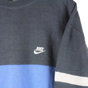 May include: A dark blue and light blue long-sleeved shirt with a white Nike logo on the front. The shirt has a white stripe on the sleeve.