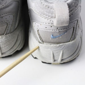 May include: A pair of gray athletic shoes with a blue Nike swoosh logo on each shoe. The shoes have a worn look and are showing signs of wear and tear.