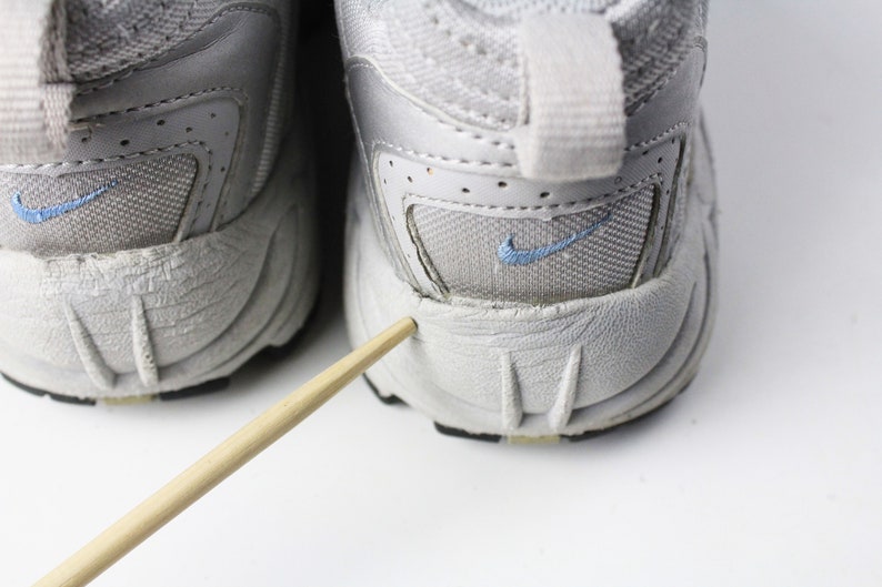 May include: A pair of gray athletic shoes with a blue Nike swoosh logo on each shoe. The shoes have a worn look and are showing signs of wear and tear.