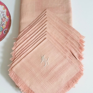 Op de afbeelding: Een set van 10 roze linnen servetten met gefranst randen. Elk servet heeft een wit geborduurd monogram "MK".