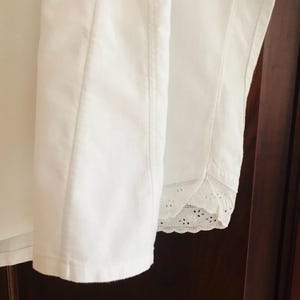 May include: White cotton shirt with a lace trim on the bottom edge. The shirt is folded and laid flat on a wooden surface.