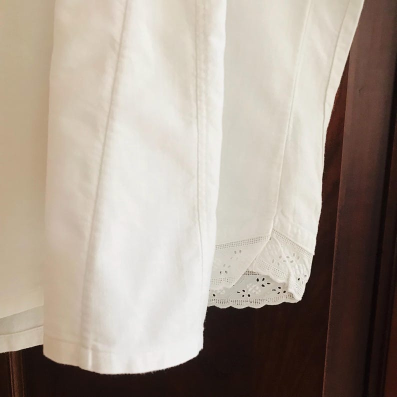 May include: White cotton shirt with a lace trim on the bottom edge. The shirt is folded and laid flat on a wooden surface.