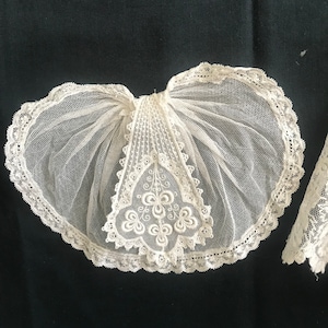 Könnte beinhalten: Ein weißer Spitzenkragen mit einem zarten Blumenmuster. Der Kragen ist aus feinem Netzstoff gefertigt und hat einen gewellten Rand.