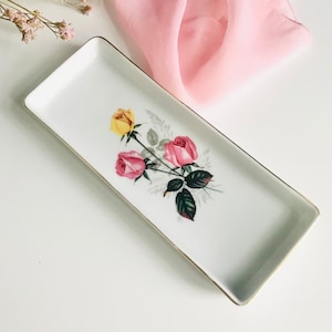 Pode incluir: Uma bandeja retangular de cerâmica branca com uma borda dourada e um design floral com rosas cor-de-rosa e amarelas.