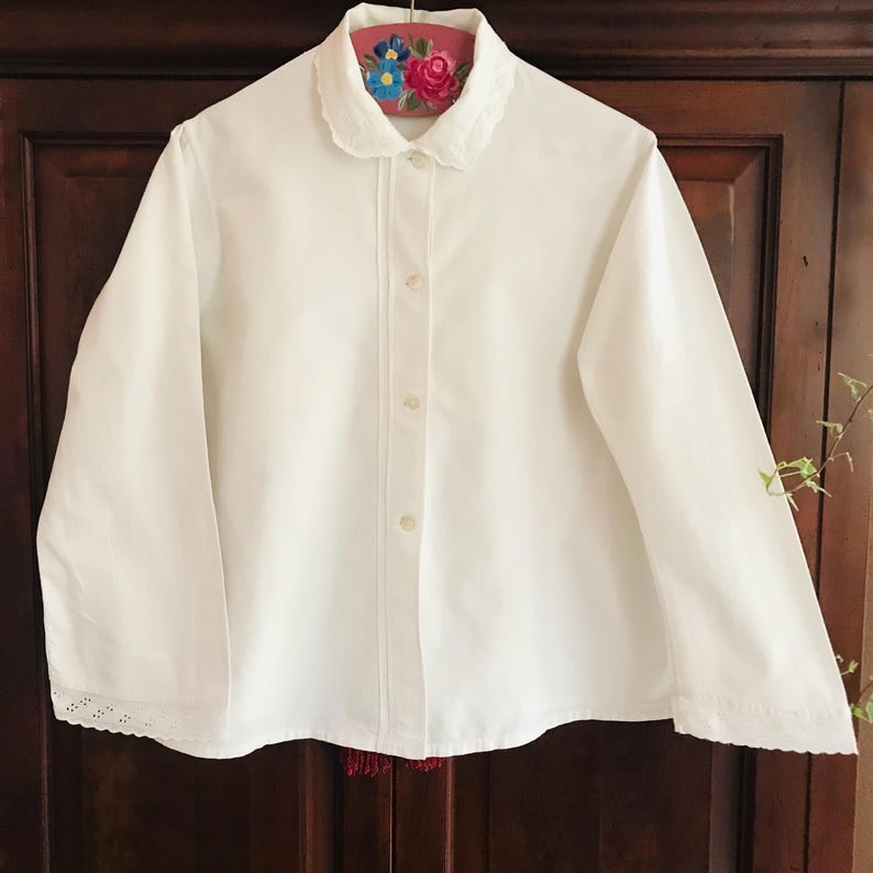 May include: A white long-sleeved shirt with a Peter Pan collar and lace trim on the cuffs. The shirt has a button-up front and is made of a lightweight fabric.