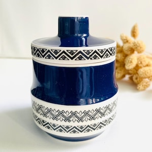 Op de afbeelding: Een donkerblauwe keramische pot met bijpassend deksel, voorzien van een witte band rond het midden en de rand van het deksel. Beide witte banden zijn versierd met een zwart geometrisch patroon van herhalende zigzaglijnen en kruismotieven.