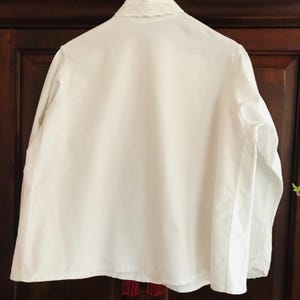 May include: A white long-sleeved shirt with a lace collar. The shirt is made of a lightweight fabric and has a relaxed fit.
