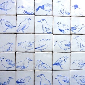 May include: A collection of 16 white ceramic tiles with blue painted bird illustrations. The birds are in various poses and styles, some with detailed markings and others with simpler designs.