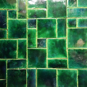 Könnte beinhalten: Eine grüne gekachelte Wand mit einem geometrischen Muster. Die Fliesen sind in einem versetzten Muster angeordnet, was ein einzigartiges und interessantes Design ergibt.