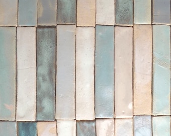 May include: A close-up of a wall made of long, narrow, rectangular tiles. The tiles are arranged in a vertical pattern and are made of a light-colored material with a subtle, mottled texture. The tiles are in shades of light blue, gray, and beige.