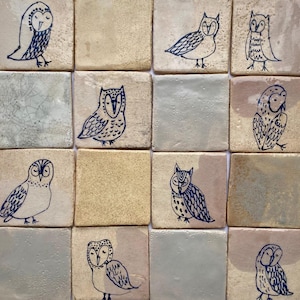 Könnte beinhalten: Eine Sammlung von sechzehn quadratischen Keramikfliesen. Jede Fliese zeigt eine einzigartige, handgezeichnete Eulenillustration in dunkelblauer Tinte. Die Fliesen haben eine Vielzahl von neutralen Farbhintergründen, darunter Beige, Grau und Off-White.